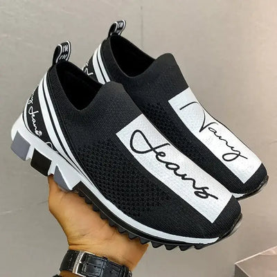 Black breathable woven sneakers with white accents and easy slip-on design, held in a hand.