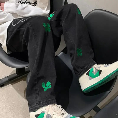 Embroidered High Street Jeans for Men featuring bold green embroidery on black denim, styled with trendy sneakers.