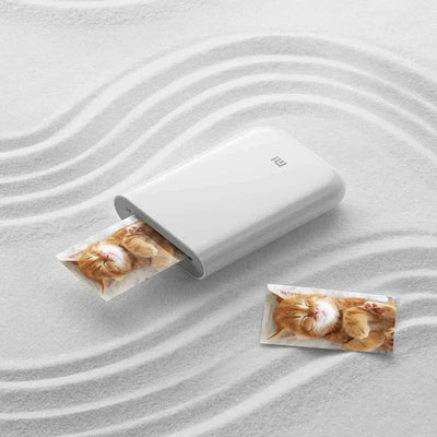 Xiaomi Mini Bluetooth Photo Printer printing adorable kitten photos on a textured surface.