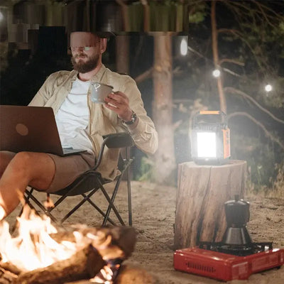 Man using High-power Energy Storage Power Supply with laptop in outdoor camping setting by the fire.